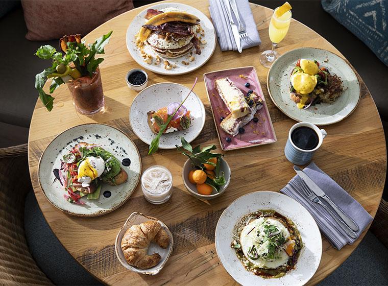 A round wooden table with a variety of breakfast dishes and drinks