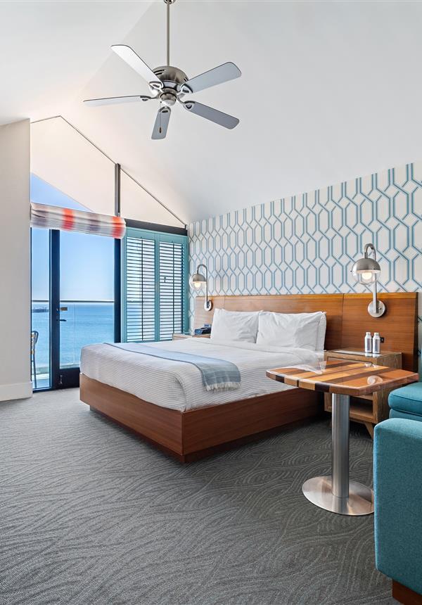 A wide view of a hotel room with a bed, desk, chair, and ceiling fan.