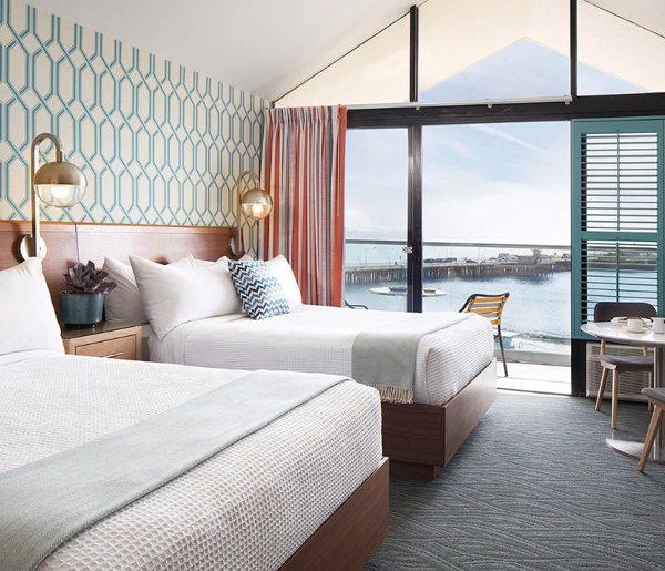 A hotel room with two beds, a desk, and a view of the water.